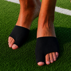 A person wearing black toe-space open-toe sandals on green turf, with a soccer ball partially visible and a yellow BESTSELLER badge in the top-left corner.